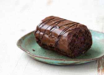 Delicious chocolate roll cake in ceramic plate on white wooden background, close up .Drunk cherry cake