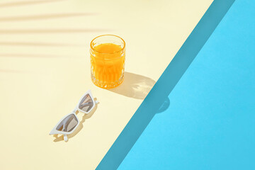 Minimal tropical composition with stylish white sunglasses and orange drink on duo tone sandy and...