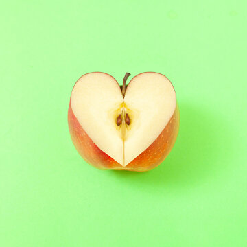 Creative composition with heart shaped sliced apple on pastel green background. Healthy lifestyle idea. Minimal nature love concept.