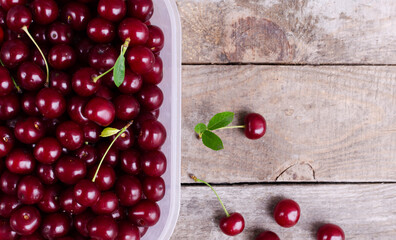 Many ripe red cherries in a plastic bowl on a wooden background. The concept of organic farming. Horizontal orientation. copy space.