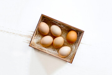 Fresh brown eggs and some straw in a wooden crate on a white background. Chicken eggs. Easter concept .Top view