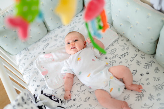 A newborn baby is lying in his bed and looking at hanging toys, a photo from above from the side of toys