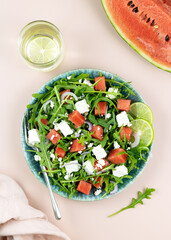Salad of watermelon, feta cheese, arugula on a pink background, top view. Summer fruit and vegetable salad.