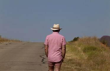 Rear view of adult man in hat walking on country road