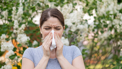 Caucasian woman suffers from allergies and blows her nose into a napkin while walking in the park. 