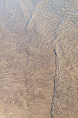 Detail close-up of wave washing onto sand beach shoreline, summer concept