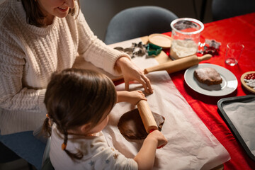 family, cooking and winter holidays concept - happy mother and baby daughter with rolling pin making gingerbread cookies from dough at home on christmas