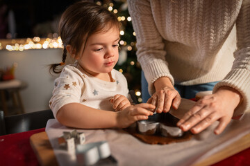 family, cooking and winter holidays concept - happy mother and baby daughter with mold making...