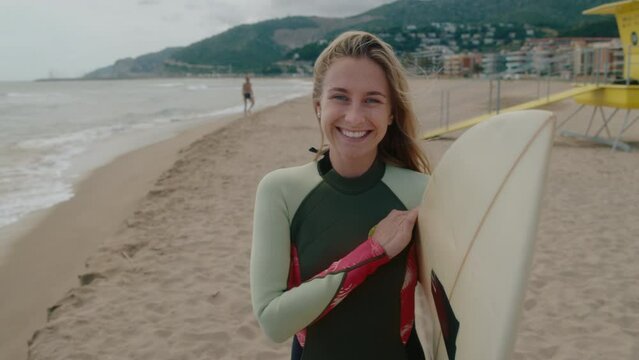 Portrait of young caucasian woman with surfboard, smile and look into camera, happy and motivated summer adventure. Surf camp in holiday resort. Surfing classes and surf vacation