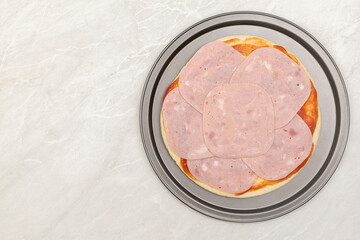 Preparing pizza dough with ketchup and ham on the top