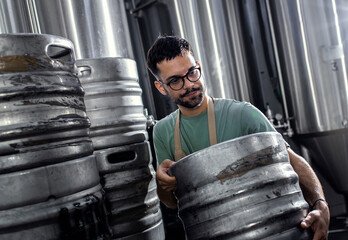 Man working in craft brewery carrying metal barrel.