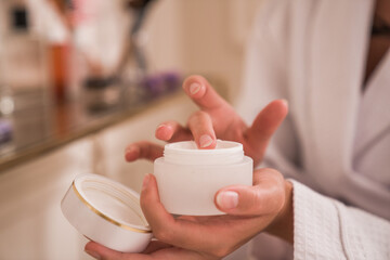 Caucasian woman is preparing applying cream for face while sitting at home during the morning