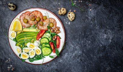 Ketogenic breakfast. Keto low carb shrimps, prawns, quail eggs, fresh salad, tomatoes, cucumbers and avocado on a dark background. keto diet. Top view