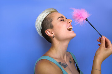 Positive tattooed woman laughing out loud while touching with pink feather stick to her nose