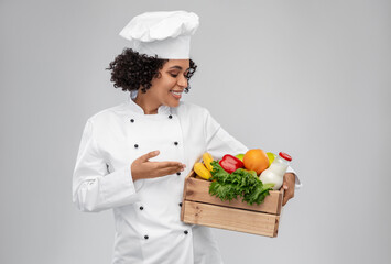 cooking, culinary and people concept - happy smiling female chef in toque holding food in wooden box over grey background