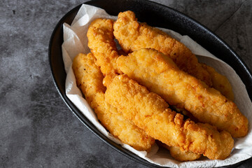 Breaded chicken fillet strips on a paper towel in a black bowl. On a concrete background