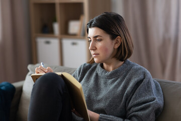 stress, mental health and depression concept - sad crying woman with diary sitting on sofa at home