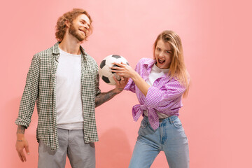 Portrait of young man and woman in casual clothes posing isolated over pink studio background. Football lovers