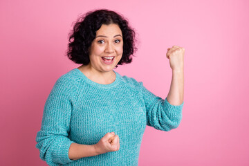 Portrait of mature woman doing a winner gesture hands up screaming yes isolated on pastel color...