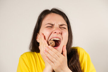 A woman gnaws on a walnut, opening her mouth wide, breaking a tooth or dislocating the temporomandibular joint, her jaw has moved away.