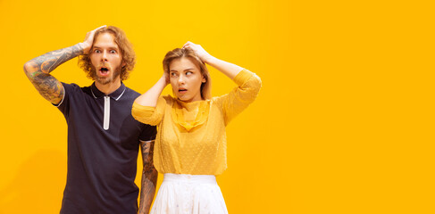 Obraz na płótnie Canvas Portrait of young man and woman in casual clothes posing isolated over yellow studio background. Showing shocked expression. Flyer
