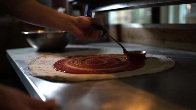 Pizza chef spreading tomato sauce on pizza base