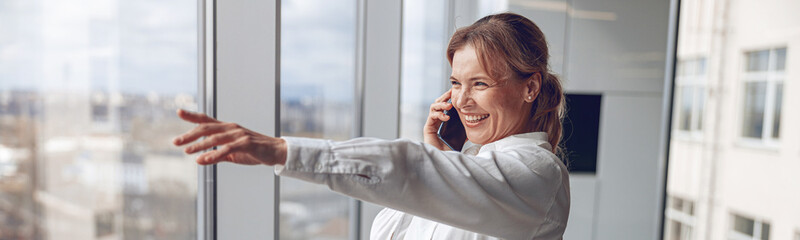 Businesswoman Making Phone Call Standing By Office Window and showing view from above.