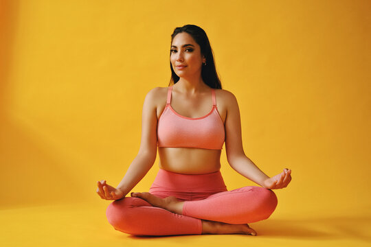 Beautiful Latina Woman Sitting In Yoga Pose In Front Of Yellow Background