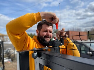 bearded smiling European man repairing sliding gates with a screwdriver