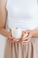 Woman in Home Clothes Holds White Candle with Wooden Lid in Her Hands. Blurred Background