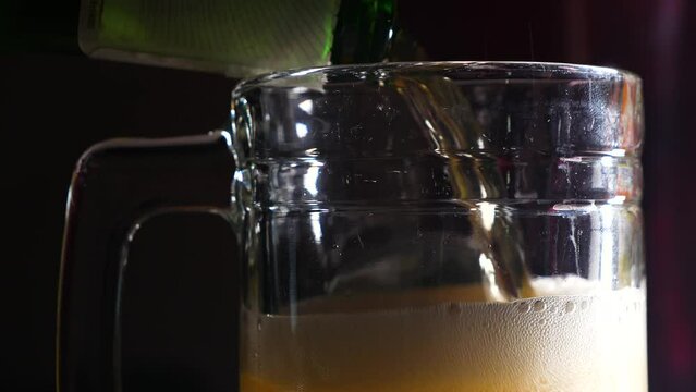 Pouring a beer into a large glass with a handle with suds on top of the adult beverage.