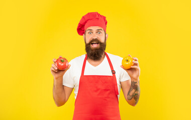 Fototapeta Surprised man in cooking apron and toque holding red and yellow tomatoes yellow background, cook obraz