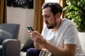 A focused man carefully reads messages received from friends about the latest developments. A man in a white T-shirt is preoccupied by what he sees after waking up from a nap.