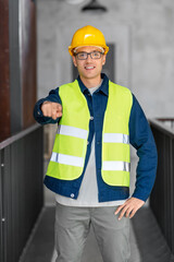 architecture, construction business and building concept - happy smiling male architect in helmet and safety west pointing to camera at office