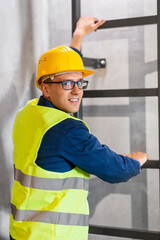 architecture, construction and building concept - happy smiling male architect in helmet, goggles and safety west climbing ladder or stairs