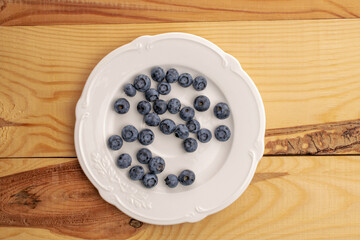 Organic blueberry berries on a white plate, close-up, on a wooden table, top view.