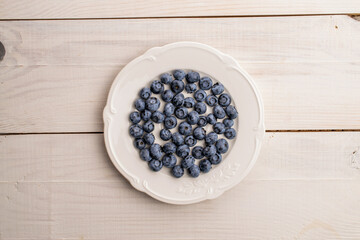 Organic blueberry berries on a white plate, close-up, on a wooden table, top view.