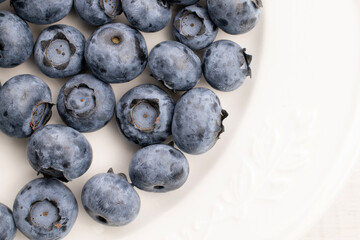 Organic blueberry berries on a white dish, close-up, top view.