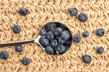 Ripe blueberries with an iron spoon, close-up, on a straw mat.