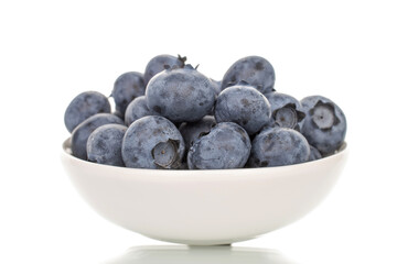 Several berries of ripe dark purple blueberries in a white ceramic bowl, close-up, isolated on white.