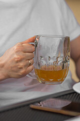 Man's hand holding a glass of beer. Married man in white t-shirt drinking tasty beer in pub.