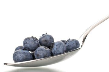 Several berries of ripe dark purple blueberries with a metal spoon, close-up, isolated on white.