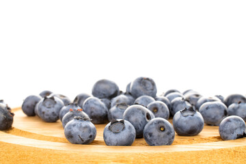 Several berries of ripe dark purple blueberries on a round tray made of wood, close-up, isolated on white.