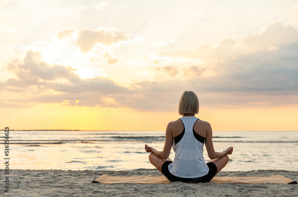 Wall mural yoga, mindfulness and meditation concept - woman meditating in lotus pose on beach over sunset