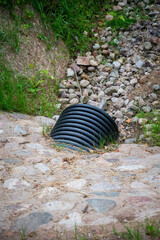Black plastic drainage culvert pipe releasing water into a stream, environmental safety issue,...