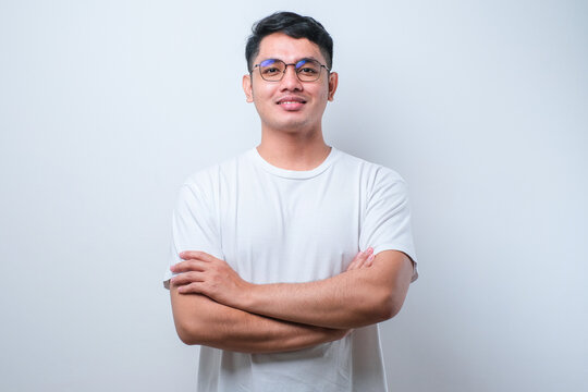 Potrait of young handsome Asian man wearing casual shirt and glasses, happy face smiling with crossed arms looking at the camera