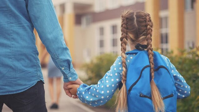 back to school. dad takes his daughter to school. schoolgirl carries go to school behind with a backpack holding hands. kid education concept. first grader going to school group lifestyle of kids