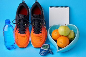 Orange sneakers, a notebook, a glucometer, a bottle of drinking water and fruits on a blue...