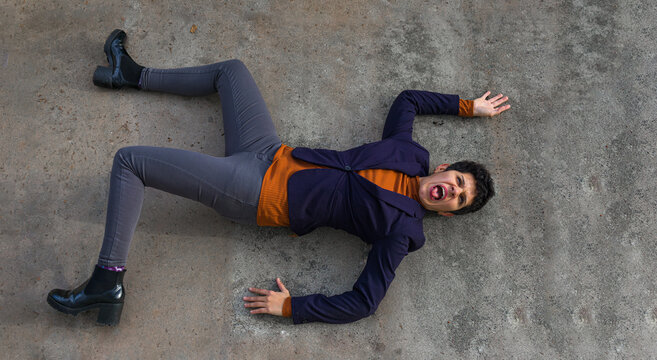 high angle view of an angry woman dressed in suit jacket and boots lying on a concrete floor while screaming