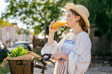 Beautiful young woman in straw hat drinks from a bottle with fresh juice at summer while with retro...